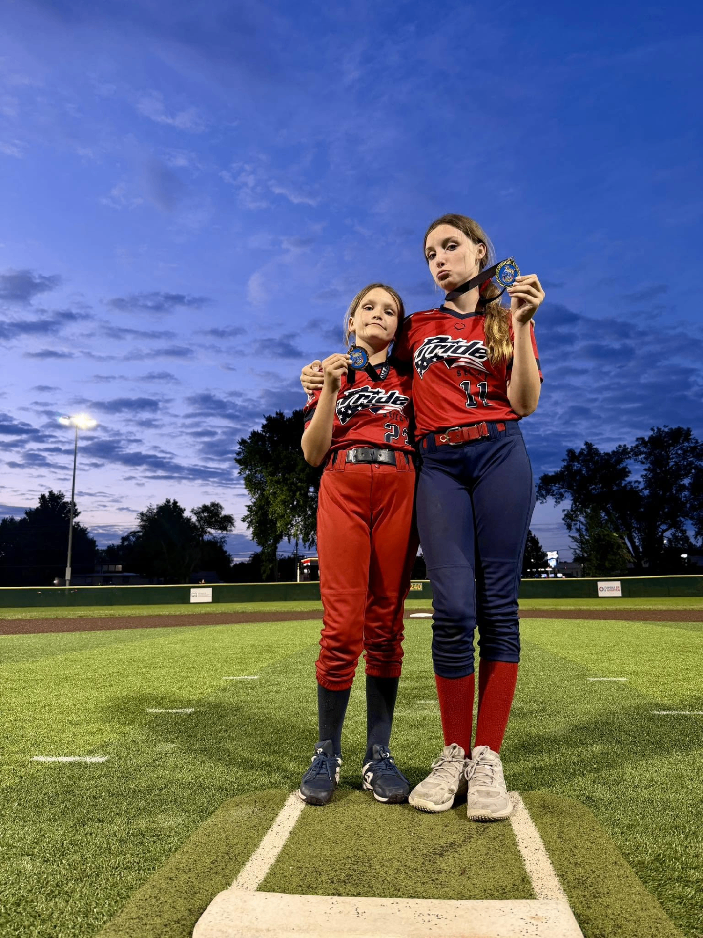 Two Pride athletes holding medals on the field at dusk